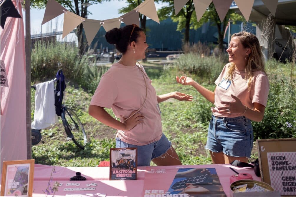 Twee vrouwen in gesprek bij een kraam op een zonnig festival